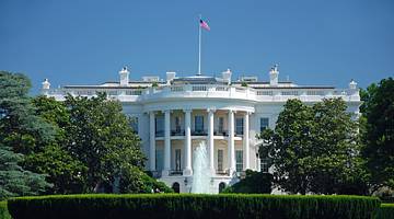 The White House with green trees surrounding it under a blue sky