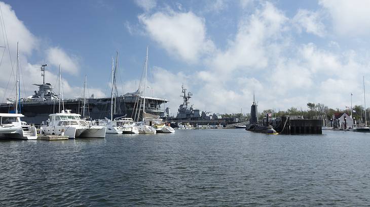 Aircraft carrier, submarine, and various boats docked in a harbor on a nice day