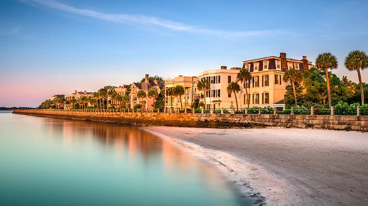 A row of antebellum mansions and palmetto trees by a beach against a colorful sky