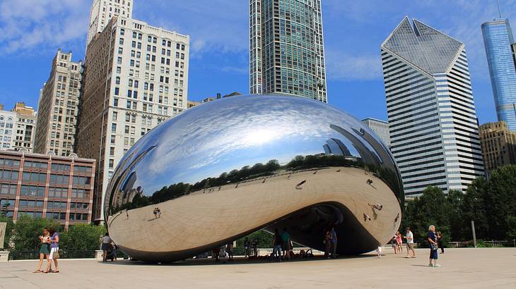 A silver reflective bean-shaped structure with high-rise buildings behind it