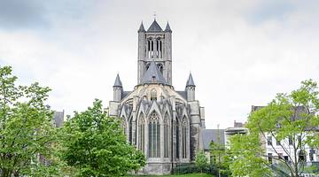 Facade of a grey Gothic church surrounded by green trees