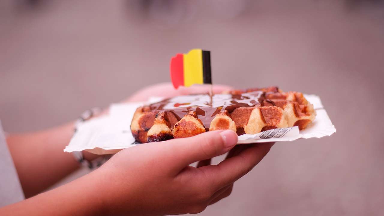 Hands holding a waffle with a Belgian flag on top