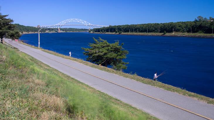 A path next to a body of water with a bridge over it and grass on the other side