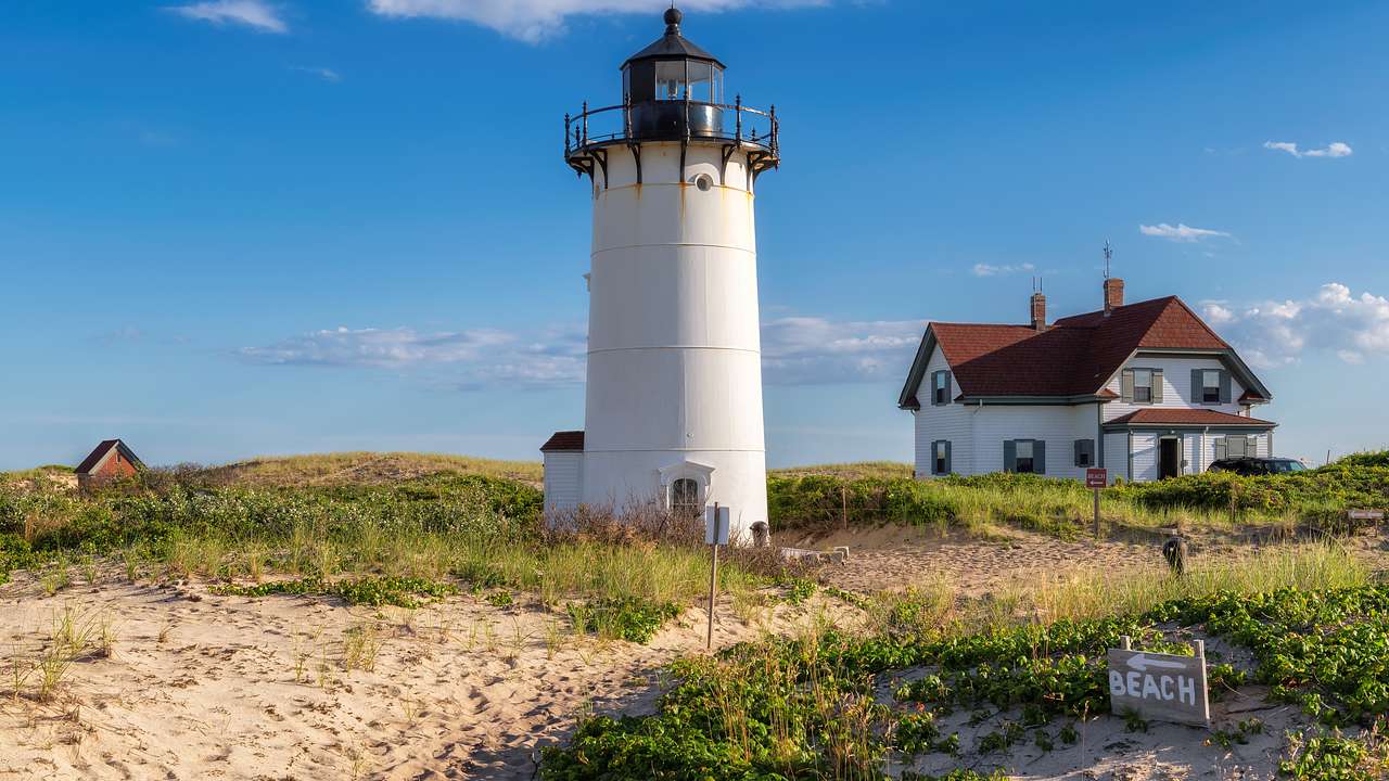 A lighthouse and small house on sand with some grass