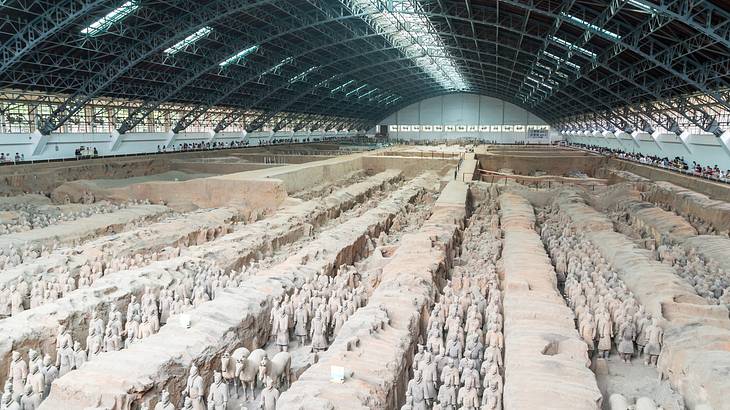 Numerous terracotta warriors, horses, and chariots in a large pit under a steel roof