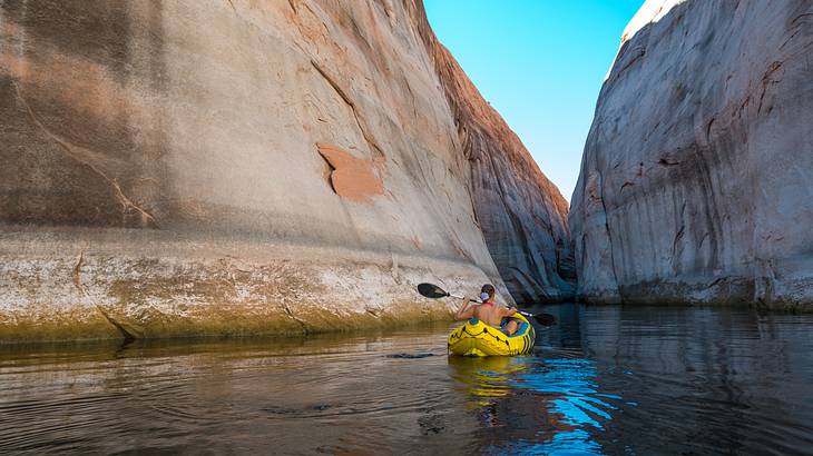 A person in a yellow kayak on a river between a rock canyon