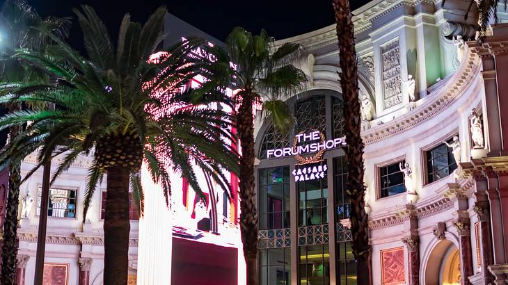A shopping mall entrance with a Forum Shops sign and palm trees in front