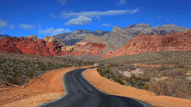 A winding road going through a desert to a red rock mountain range A winding road going through a desert to a red rock mountain range