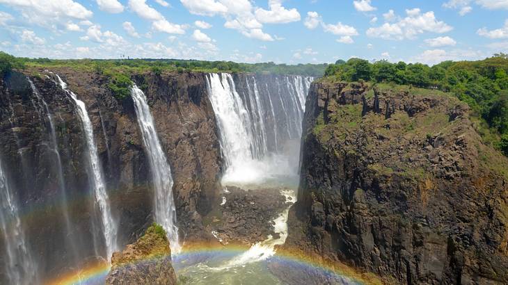 A rainbow near waterfalls rushing down green-covered rocky cliffs