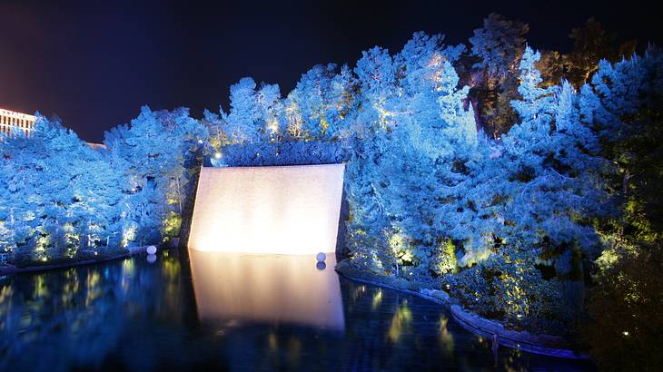 A pool at night with trees and a white monument lit up