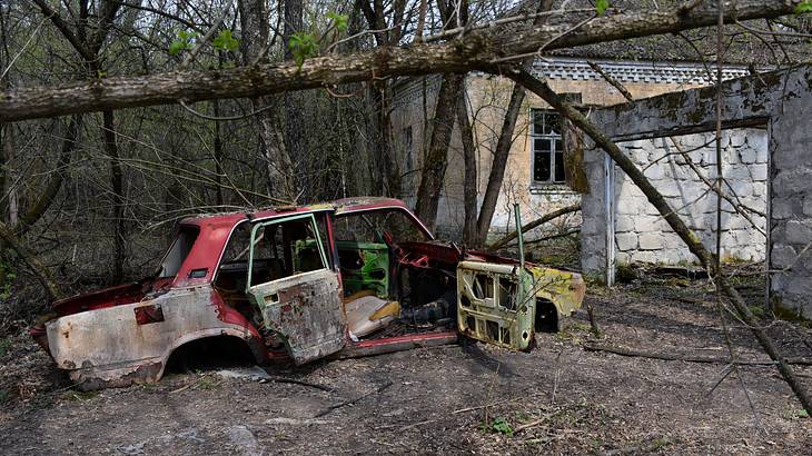 A broken old rusty car near an abandoned dilapidated house