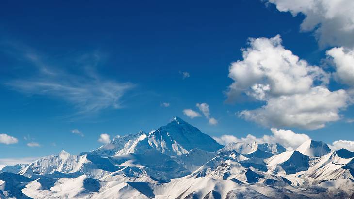 Panoramic view of snow-covered mountains against a blue sky with white clouds