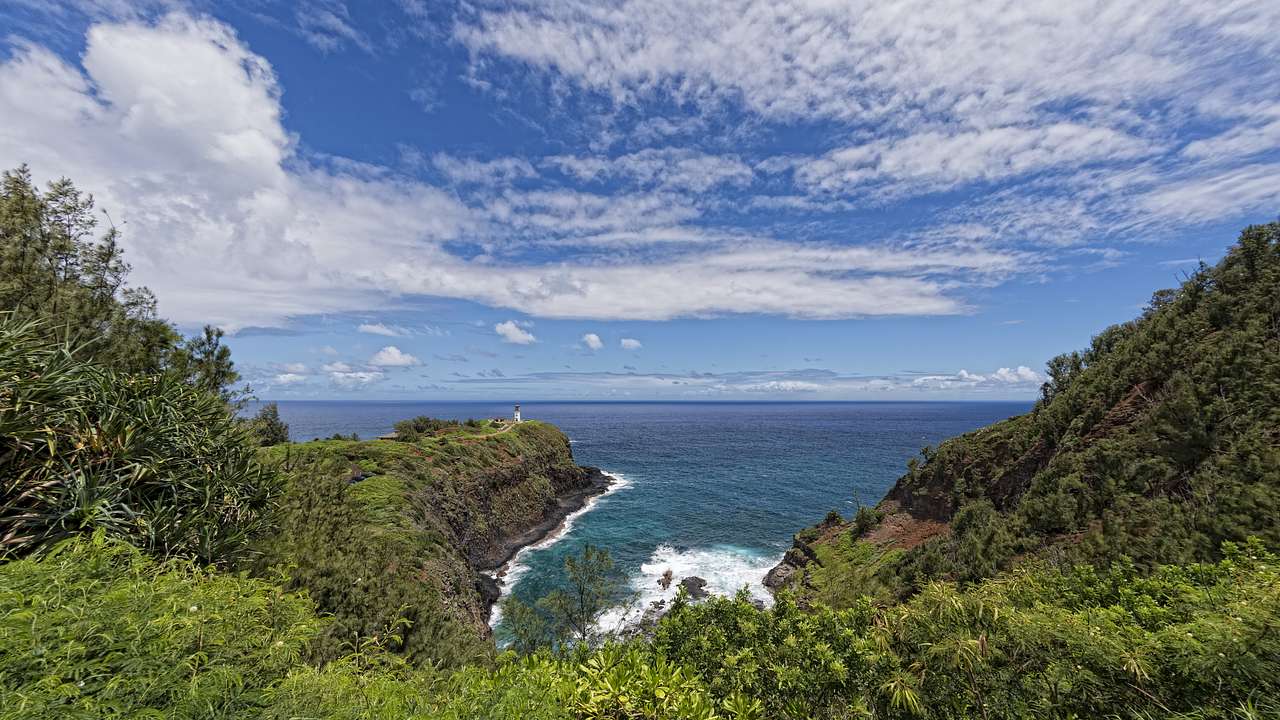 Greenery-covered cliffs with the ocean beside them under a blue sky with clouds