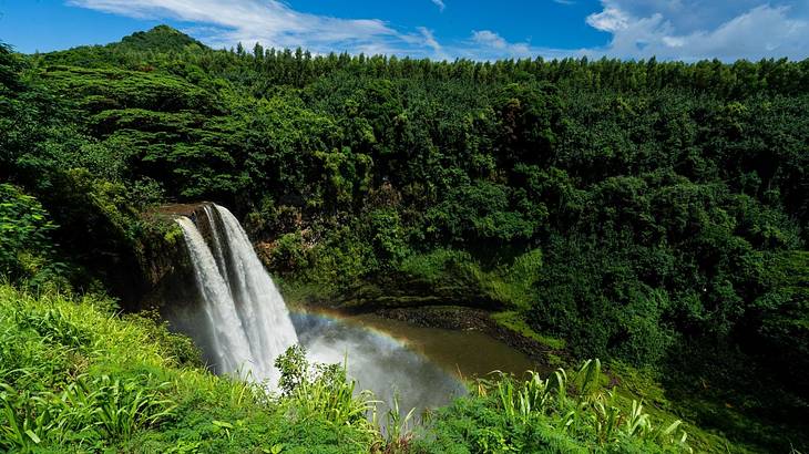 A double waterfall with a pool below surrounded by greenery-covered mountains