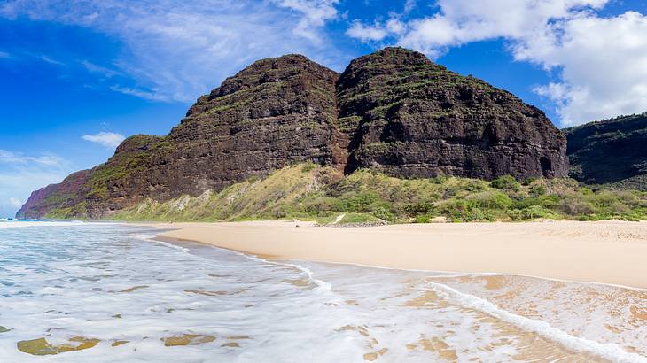 Ocean waves flowing onto and with a cliff in the background under blue sky