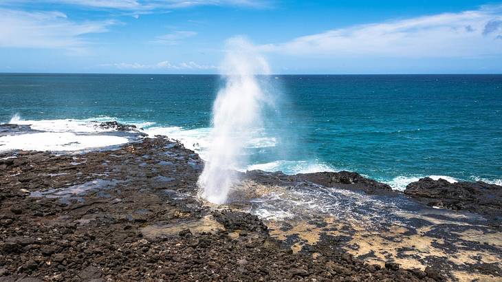 Seawater spouting into the air out of volcanic rocks with the sea in the back