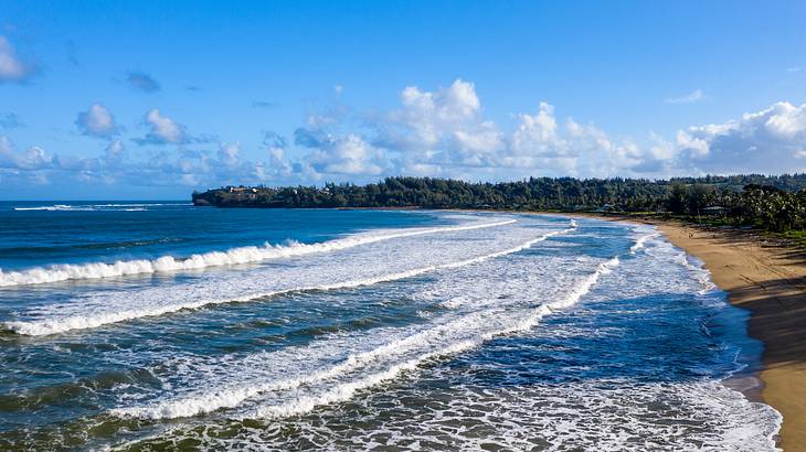 Ocean waves gently crashing onto a sandy shore under a blue sky with clouds