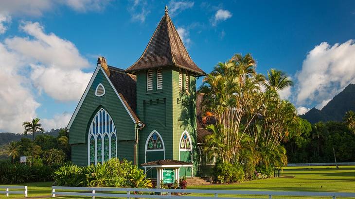 A small green church with white windows surrounded by grass and green trees