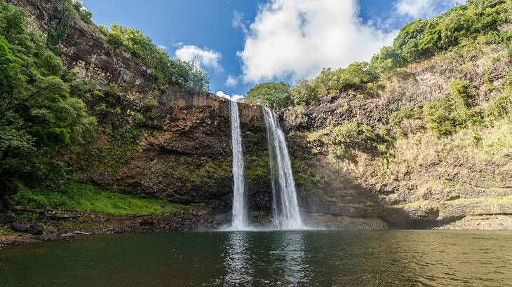 A twin waterfall flowing into a pool below with rock cliffs surrounding it