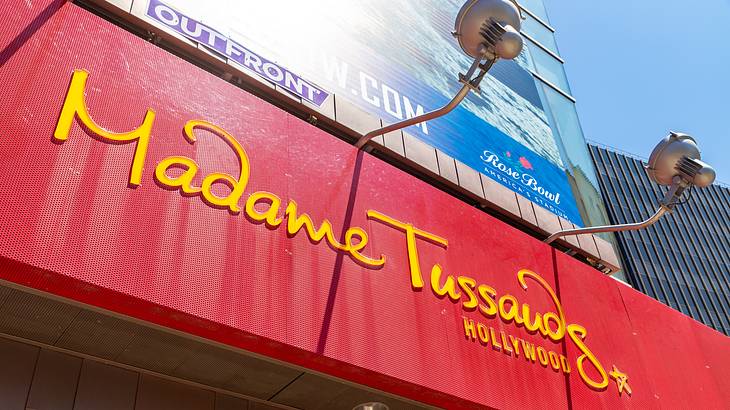 A red signboard with a yellow Madame Tussauds sign from below