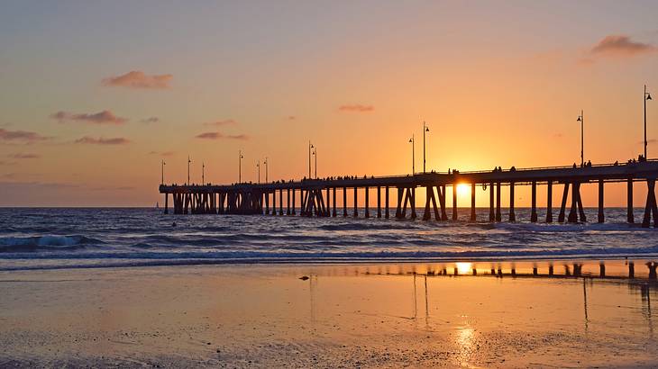 The sun setting in the background of a long boardwalk along the beach