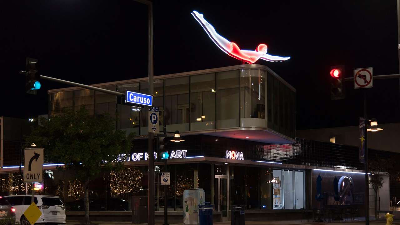 A lit-up neon sign of a diver atop a two-storey building at night