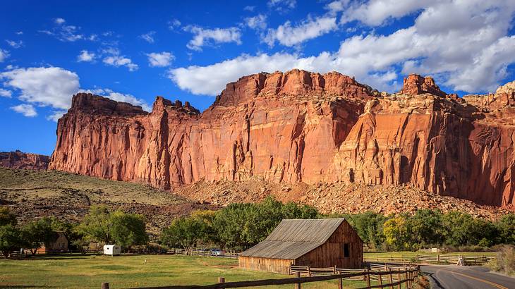 Stunning view of a fenced barn along a road with a huge cliff and trees behind