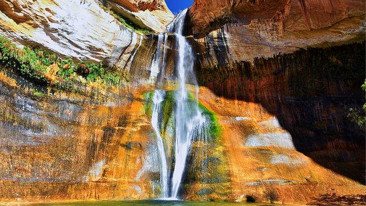 Tall skinny waterfall with colorful rocks and moss falling into a pool below