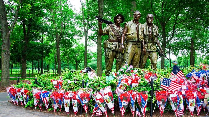 Statue of three soldiers with greenery, flower bouquets, and US flags surrounding