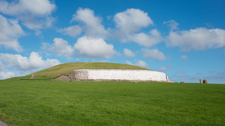 A passage of tombs on a green hill against a partly cloudy sky