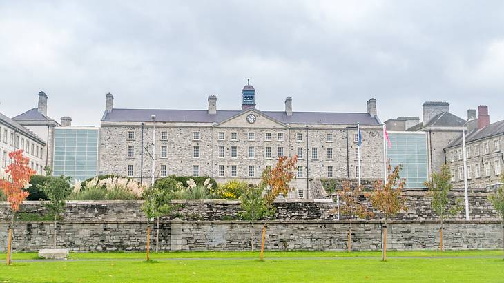 Flagpoles and a grassy lawn in front of a grey building with a clock Flagpoles and a grassy lawn in front of a grey building with a clock