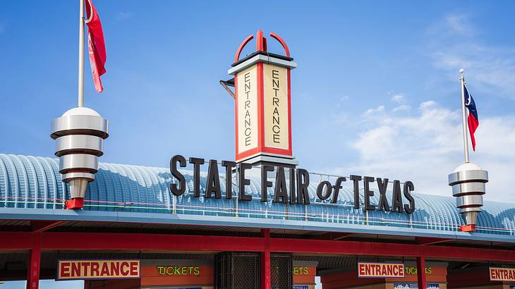 The entrance to a fair with a "State Fair of Texas" sign and red flags