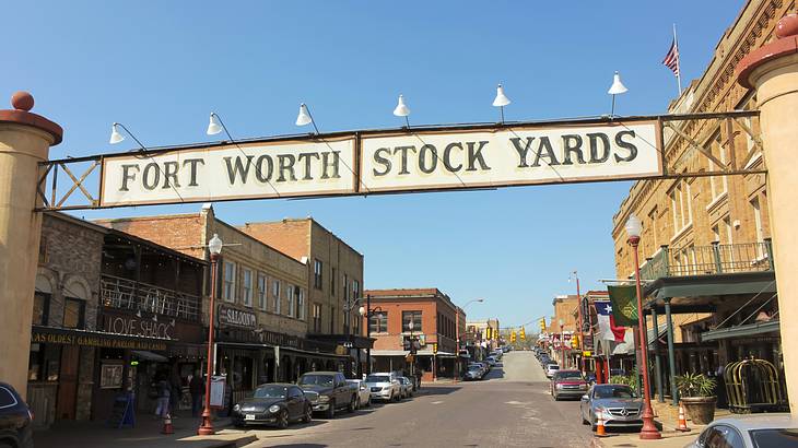 A sign that says "Fort Worth Stockyards" over a street with cars and buildings