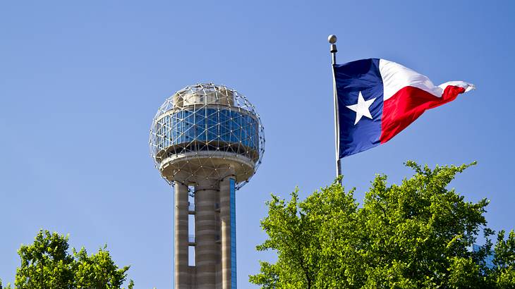 A tower with a round observation deck on the top and a Texas flag next to it A tower with a round observation deck on the top and a Texas flag next to it
