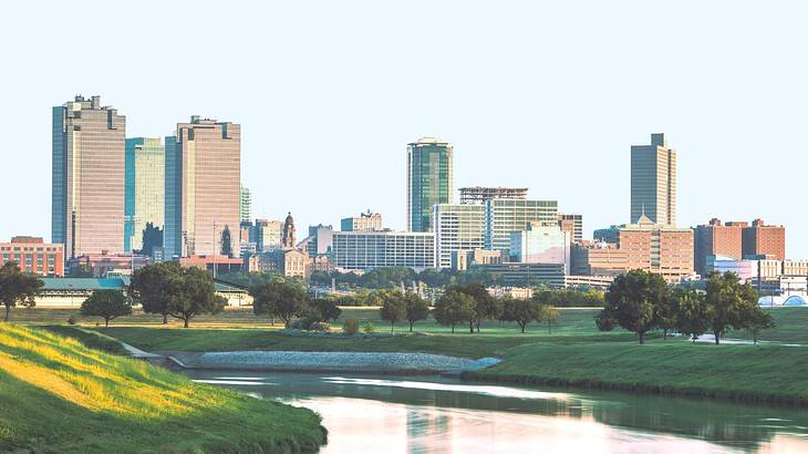 A city skyline with a river and green grass in front of it
