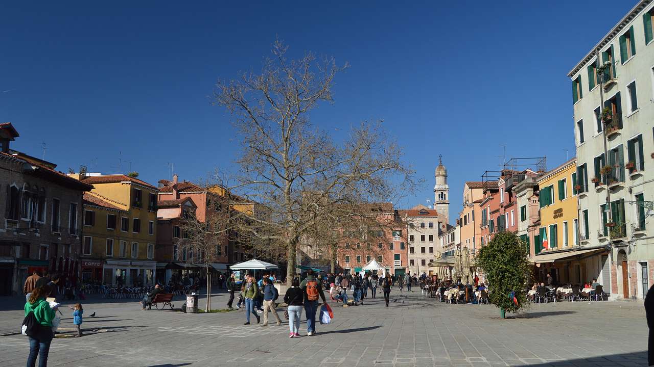 People roaming on a square with colorful buildings around, under a blue sky