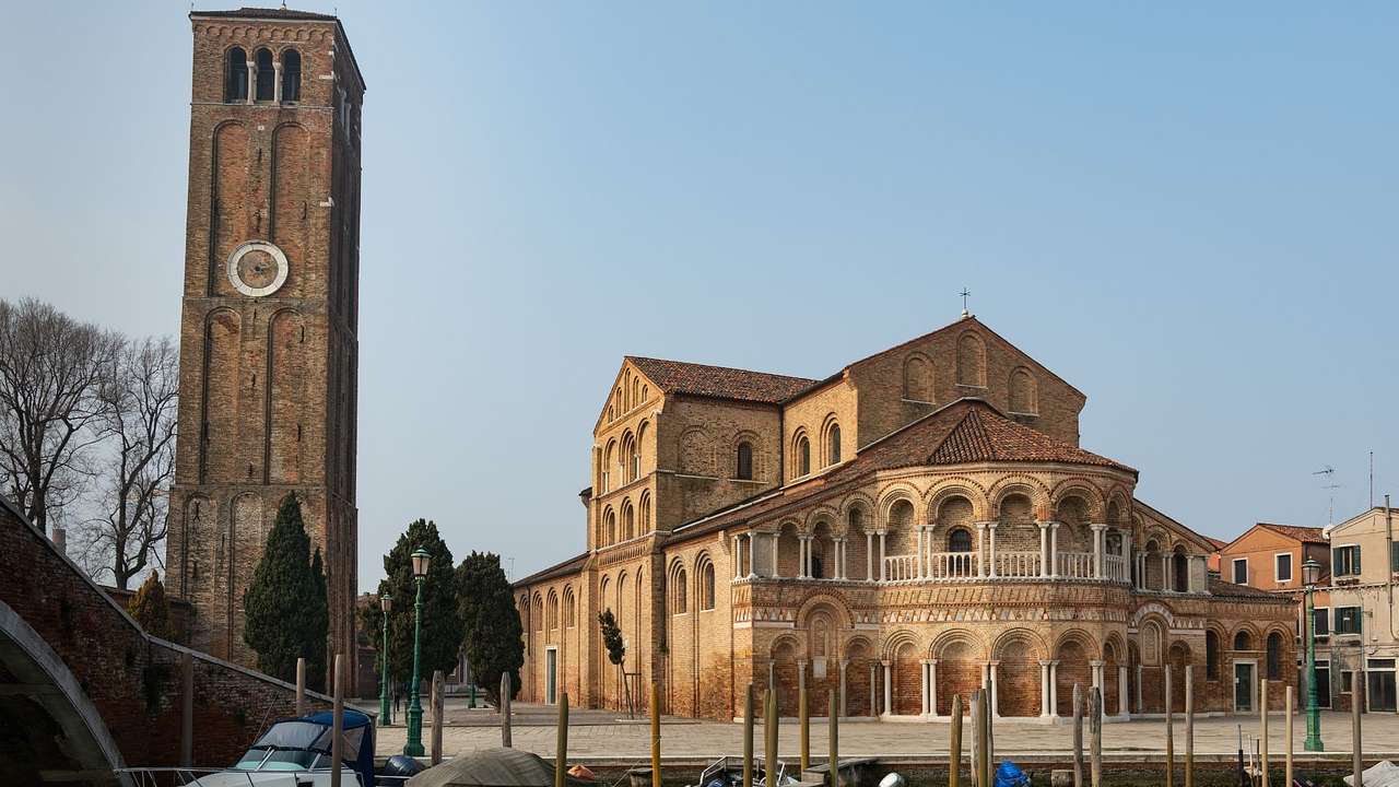 Boats moored in front of a Romanesque church with a bricked tower next to it