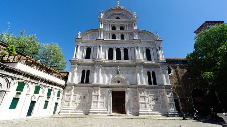 White stone-colored church with trees nearby, under a clear blue sky