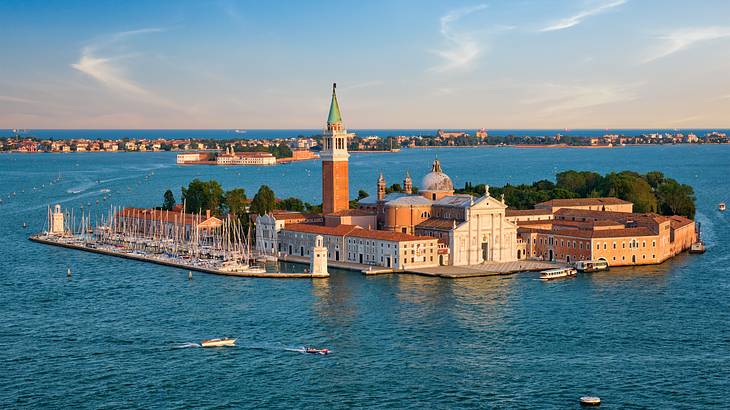 Under a blue sky, a little island with a white church, buildings, and a tower