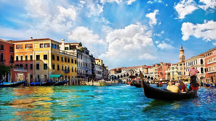 Tourists riding a gondola on a canal with houses and a bridge behind