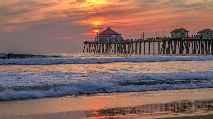 Waves breaking on a sandy beach with a pier in the distance during sunset
