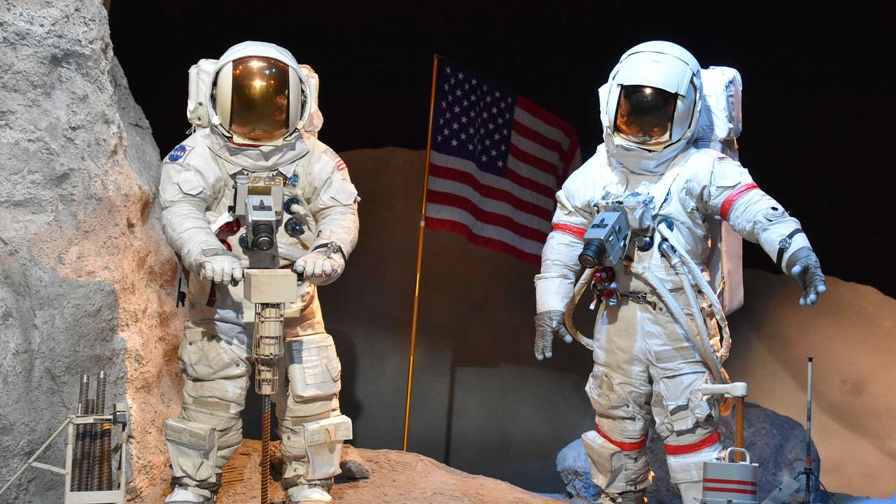 Mannequins in spacesuits and helmets in an exhibit with a red, white and blue flag
