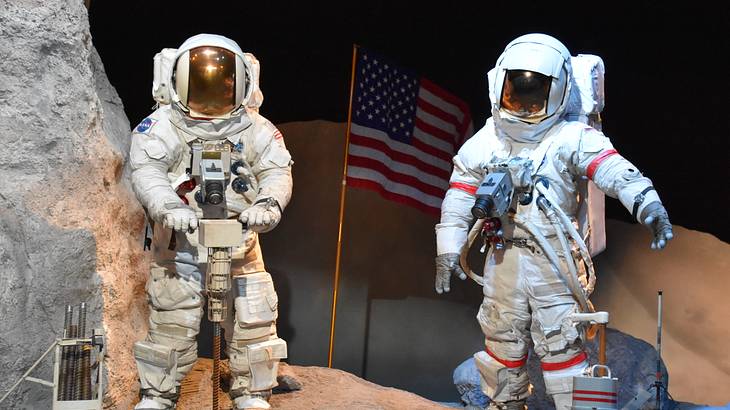 Mannequins in spacesuits and helmets in an exhibit with a red, white and blue flag