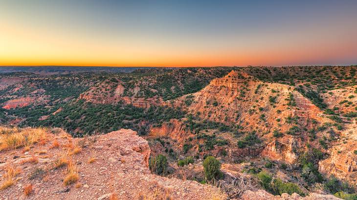 Aerial of a sunrise over a cliff, overlooking mountains with dry plants