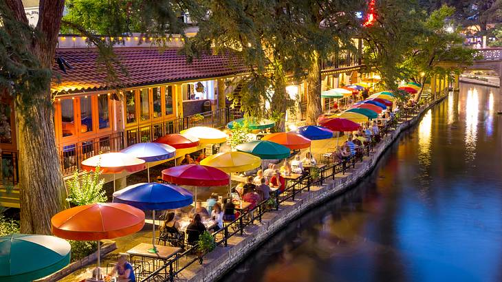 Aerial of people sitting under colorful umbrellas along a river