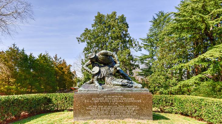 Statue of a soldier holding a man in his arm on a rectangular base, in a garden Statue of a soldier holding a man in his arm on a rectangular base, in a garden