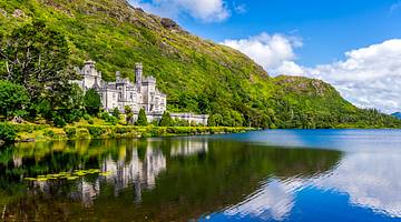 An abbey at the foot of a green mountain reflected in a lake