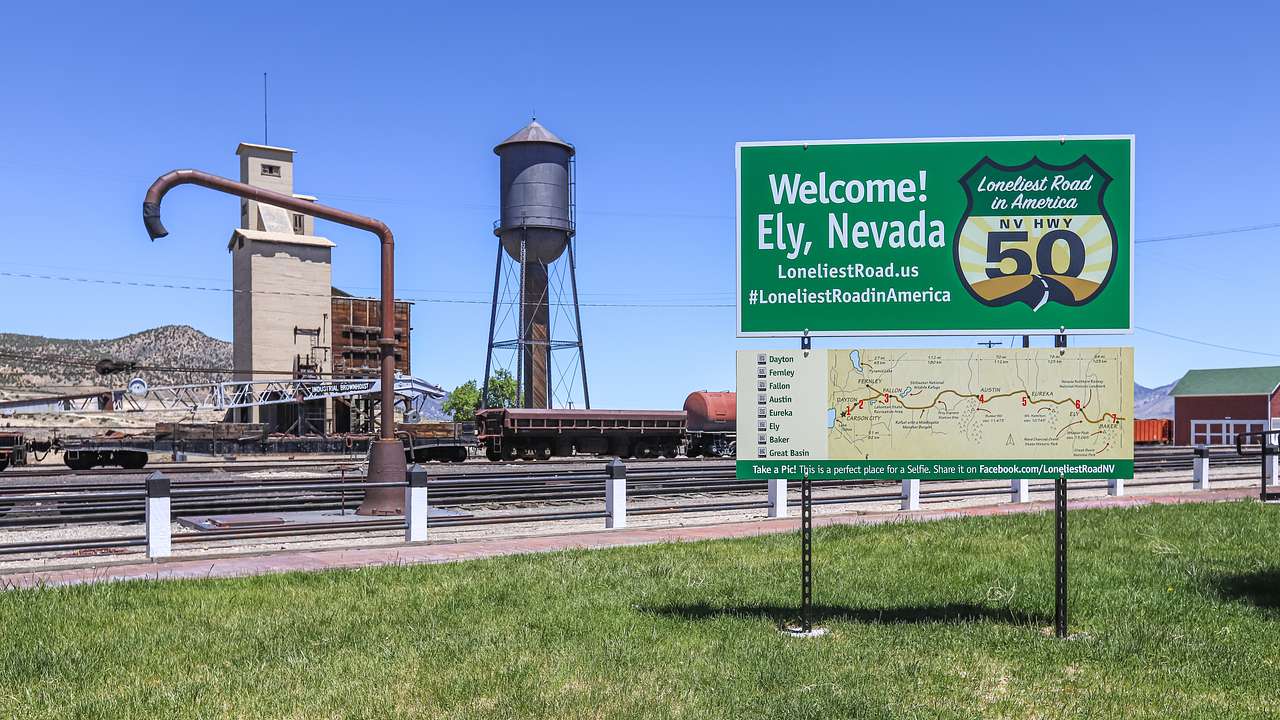 A large gray water tank and a green welcome sign with a map on a green lawn