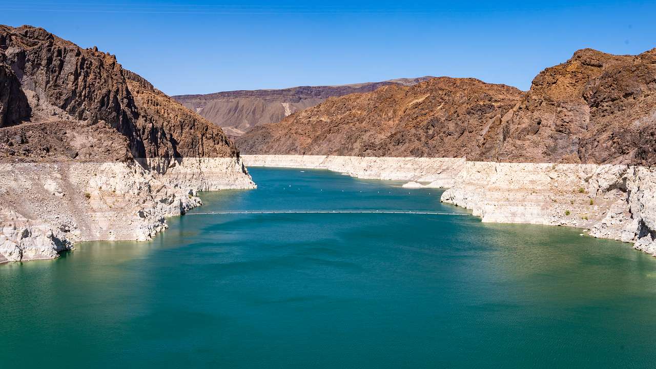 Clear blue sky and a lake with green water surrounded by dry mountains