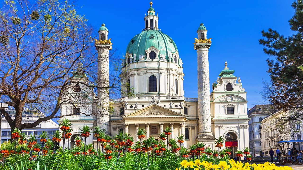 A large white baroque church with a teal dome and two towers, behind flowers